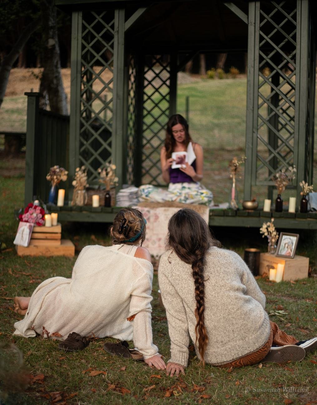 Guests on the grass listening as Rachael Ball reads under a gazebo strung with candles.