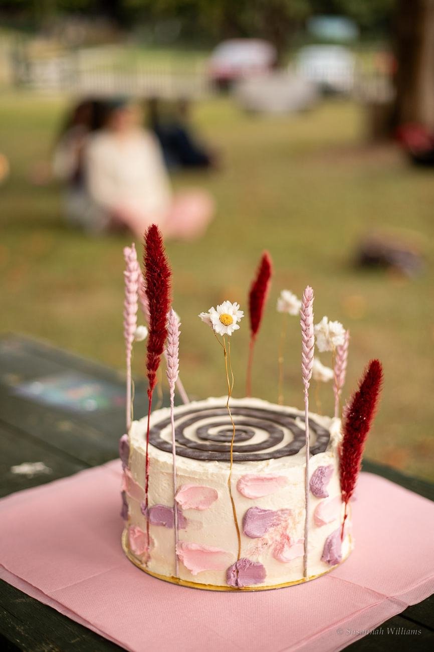 A cake decorated with dried flowers and pink and purple frosting.