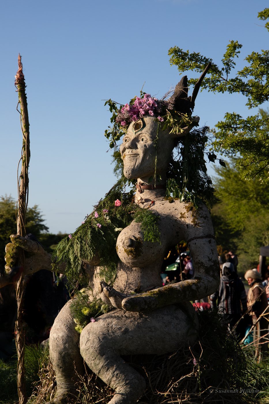 A stone goddess sculpture dressed with flowers, greenery and horns.