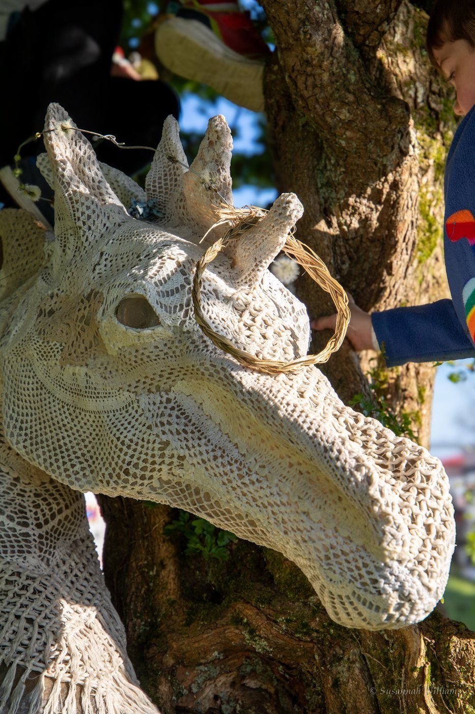 A horse head sculpture covered in white lace with a braided straw ring on one ear.
