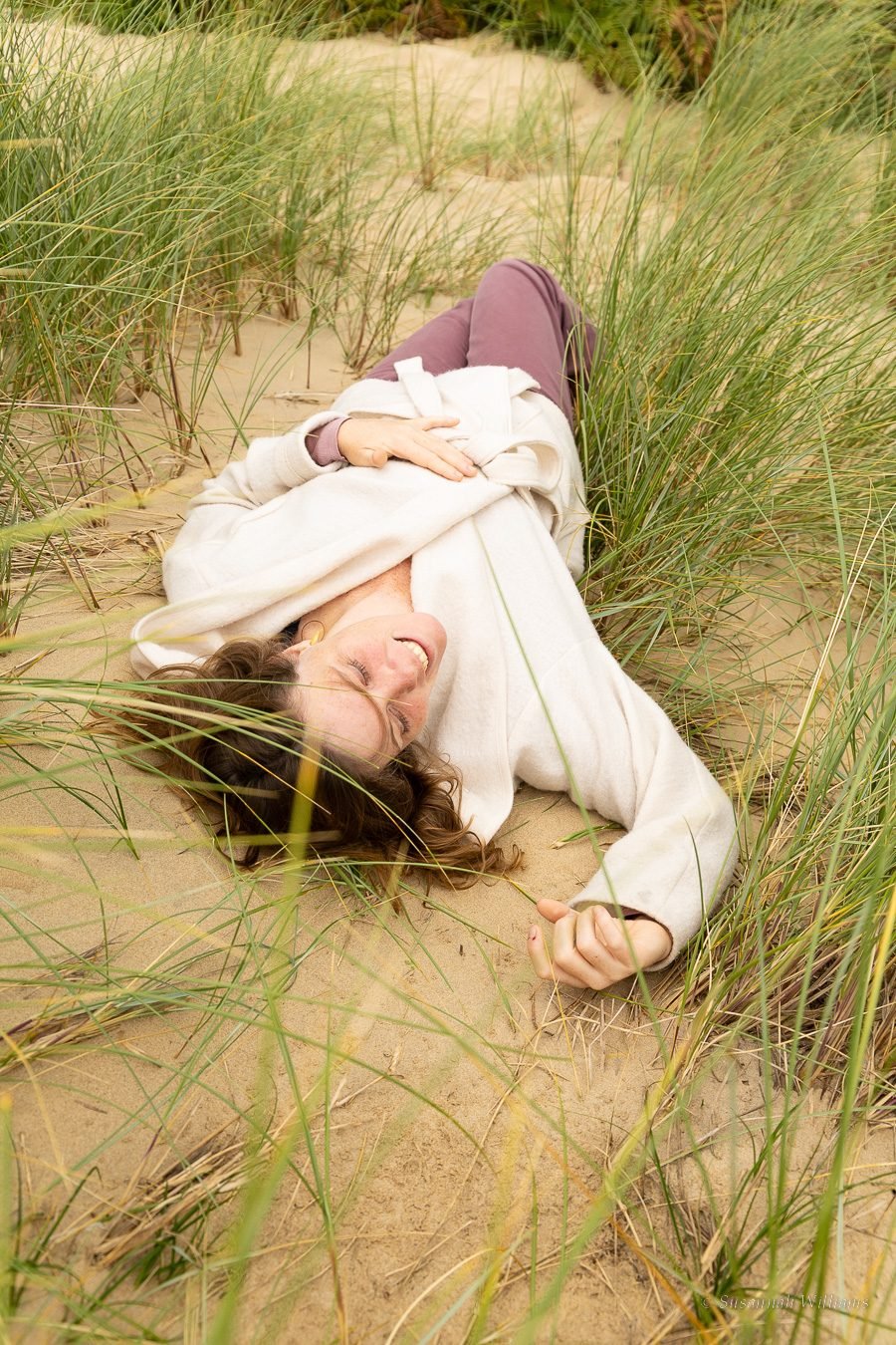 Lying in the dunes among the grass, smiling with eyes closed.