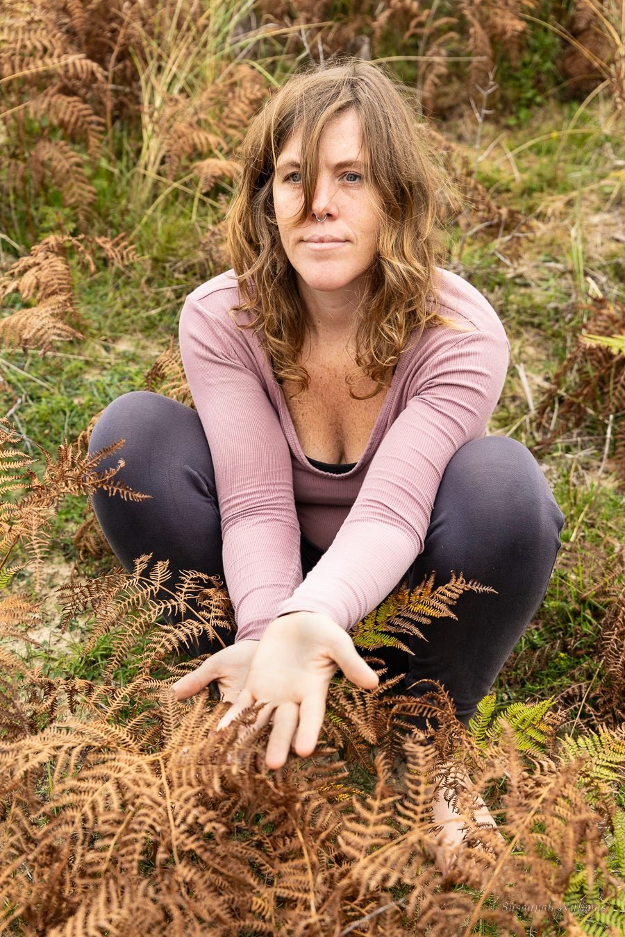 Sitting among copper bracken, hands held out towards the camera.