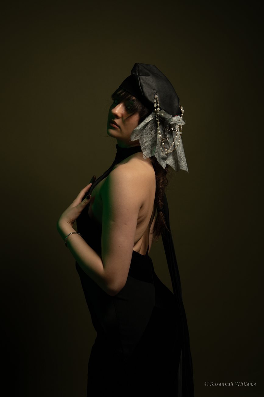 A woman beneath a pearl-studded white net veil, strands of pearls wrapped around her hand.