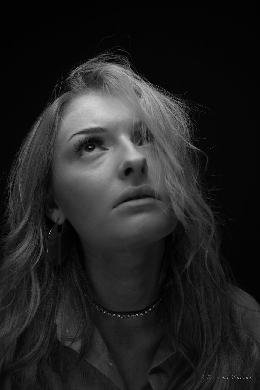 A black and white portrait of a woman with long wavy hair falling across her face, looking up.