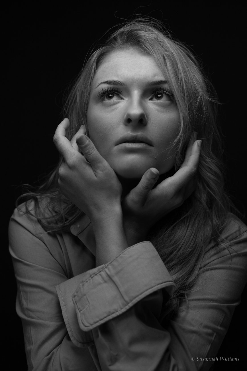 A black and white portrait of a woman looking upward, her hands cupped around her face.