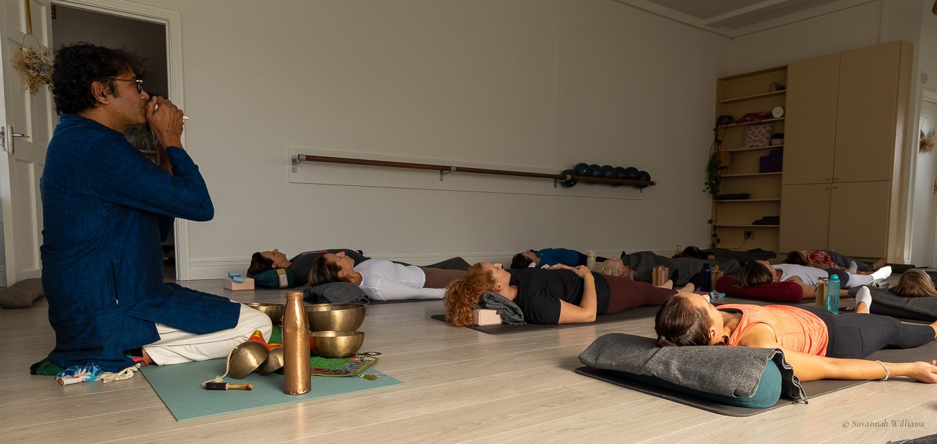 Parag kneeling at the front of the room with his bowls as everyone lies on their mats for the sound bath.