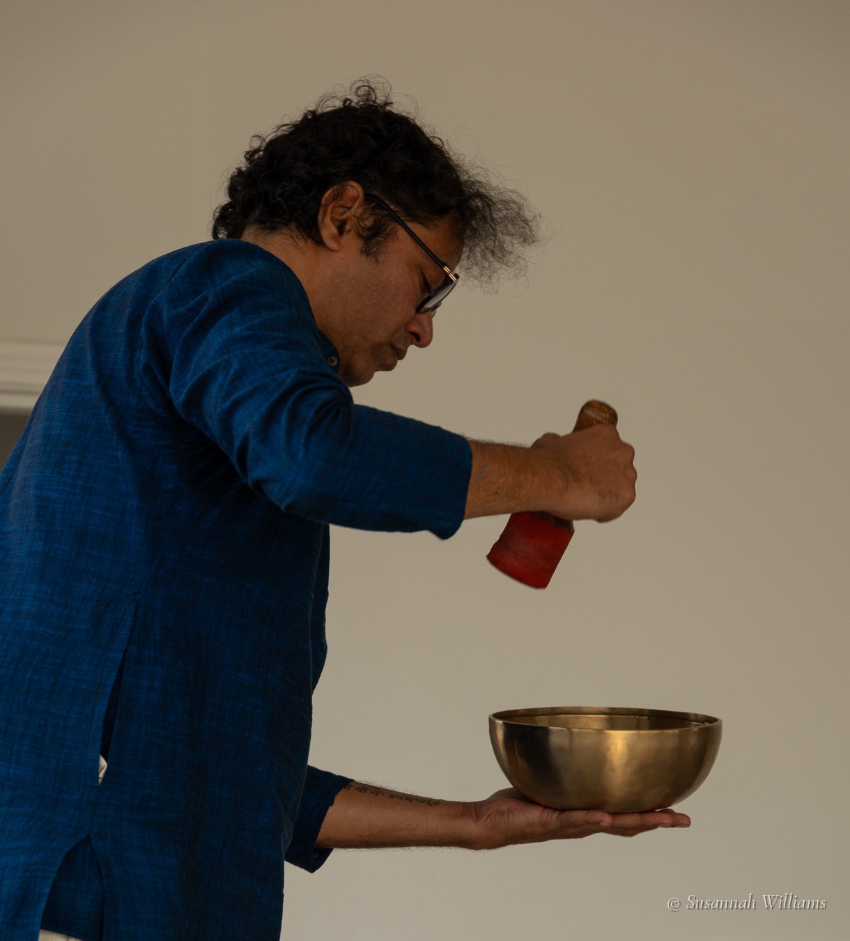 Parag in profile striking a singing bowl balanced in his palm with a red mallet.
