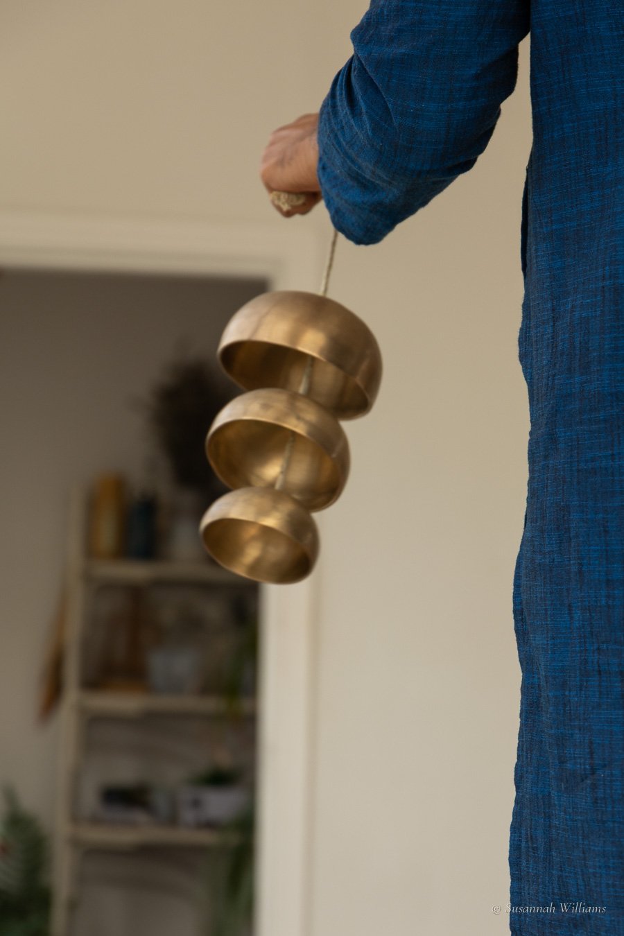 Three brass bells hanging from Parag's hand, framed by the doorway behind.